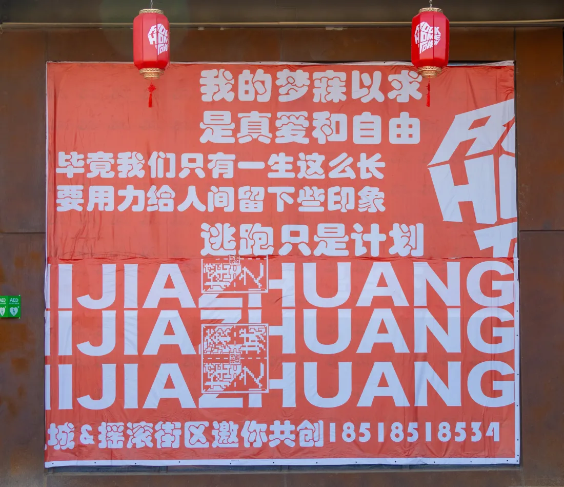 一张挂在城市街头墙壁上的巨大红色横幅,上面用醒目的白色大字写着标语“我的梦寐以求是真爱和自由”、“要用力给人间留下些印象”等,充满了态度和艺术感。